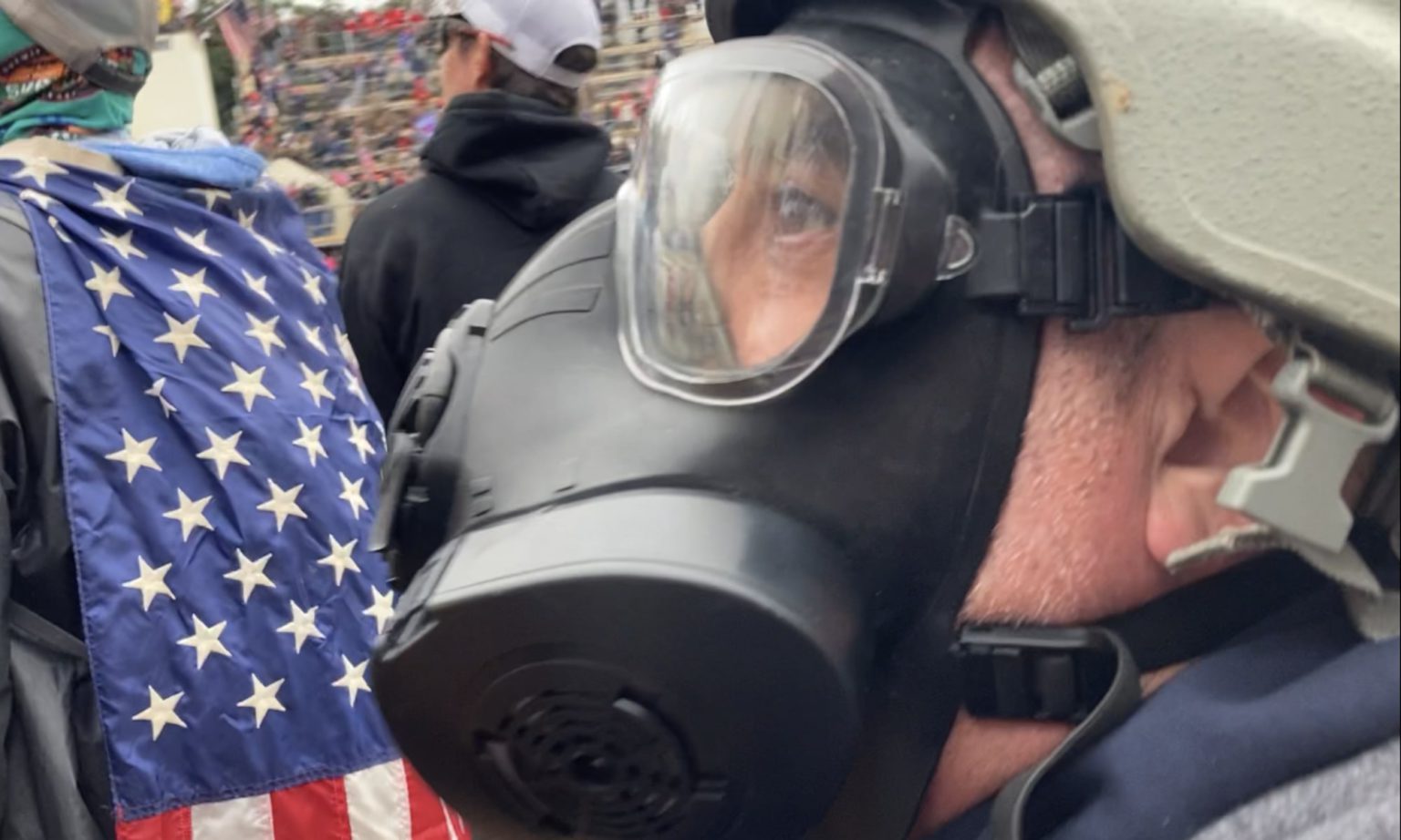 A man in a helmet and gas mask gazes up at the US Capitol. Washington DC, 6 January, 2021.