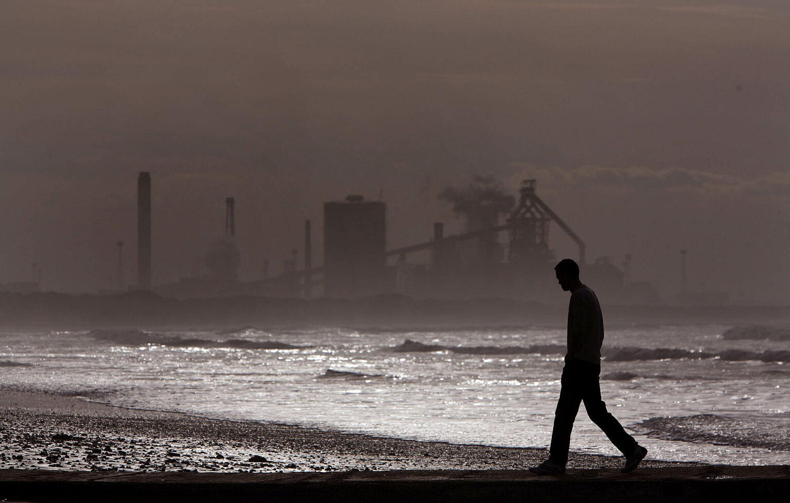 A man walks along Redcar beach in the shadow of the Corus Steelworks in Teeside, 21 July 2008.