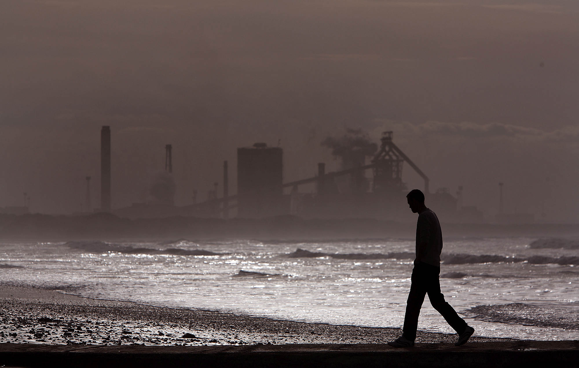 A man walks along Redcar beach in the shadow of the Corus Steelworks in Teeside, 21 July 2008.
