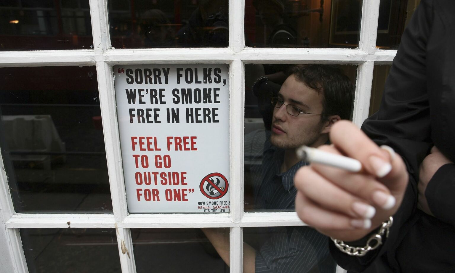 A barman adjusts a sign in the window of the Saracens Head public house on 30 June 2007 in Bath, England in preparation for the smoking ban.