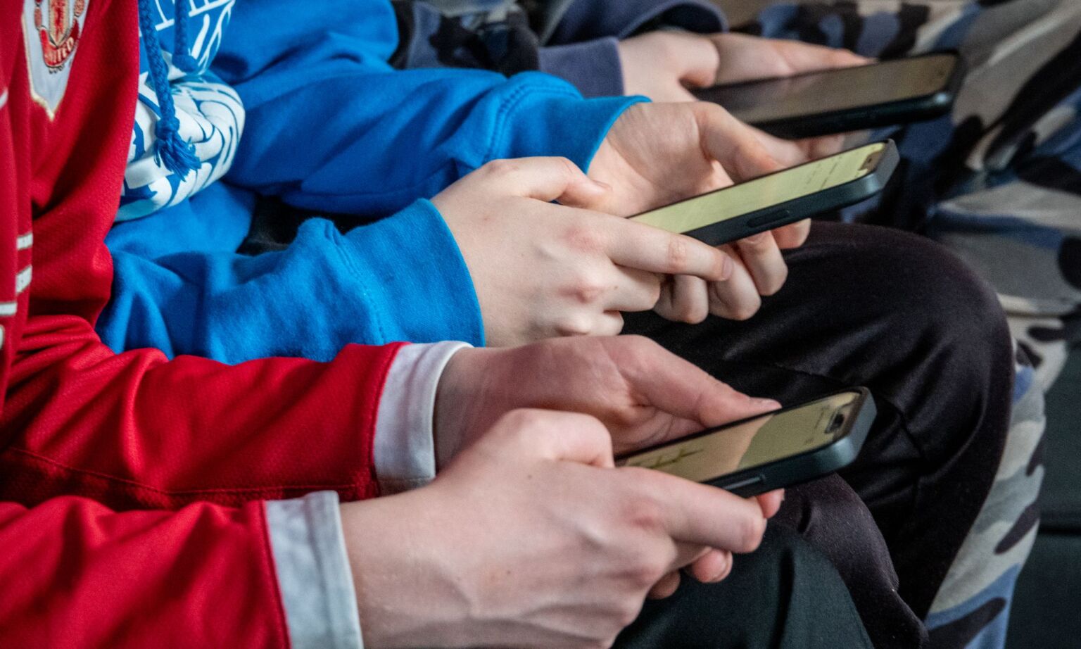 Three teenagers look at their smartphones.