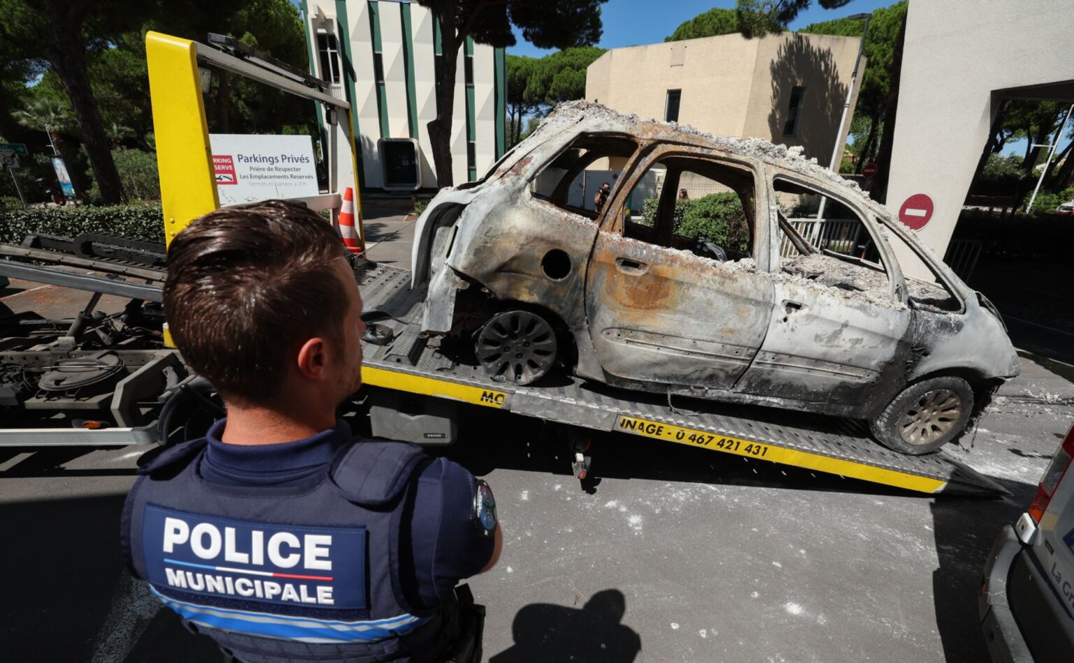 A Police officer stands in front of a car set on fire during the attack on the Beth Yaacov synagogue in Montpellier, France, 26 August 2024.